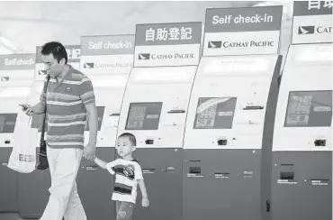  ??  ?? A man and a boy walk past Cathay Pacific’s self checking booth at the airport in Hong Kong. The airline says it expects the cargo market to improve, but did not provide a timeframe. — AFP