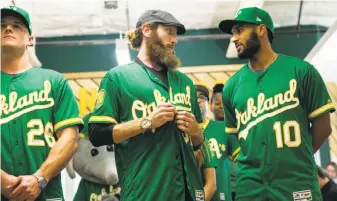  ?? Jessica Christian / The Chronicle ?? From left, third baseman Matt Chapman, former pitcher Dallas Braden and shortstop Marcus Semien model the new 1970s-esque alternate jerseys at the team’s Jack London Square offices.