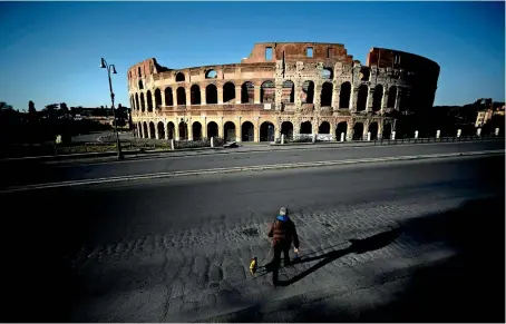  ?? AFP ?? DESERTED LANDMARK : A man walks his dog in front of the Colosseum in central Rome, during the country’s lockdown aimed at curbing the spread of the Covid-19 infection. —