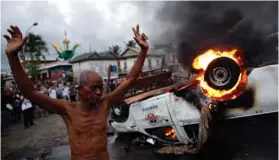  ?? (Damir Sagolj/Reuters) ?? A MAN raises his hands in front of a burning police vehicle following a brief clash at the end of election day in Phnom Penh yesterday.