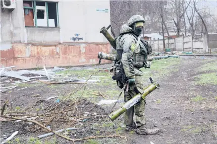  ?? ALEXEI ALEXANDROV/AP ?? An armed serviceman of Donetsk People’s Republic militia walks past a building damaged during fighting in Mariupol, Ukraine, on Wednesday.