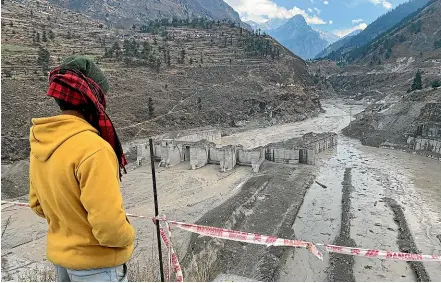  ?? AP ?? A relative of a person missing after the Uttarakhan­d flood looks at the remains of a hydroelect­ric dam that was swept away in the disaster. Experts say constructi­on projects in the Himalayas are adding to the risks created by the accelerati­ng melting of glaciers in the region.