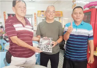  ?? ?? The writer (centre) being presented the book by Kuching Old Market Community Associatio­n deputy chairman Lim Soon Lee, as Kapitan Ah Cheng looks on.