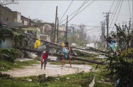  ?? DESMOND BOYLAN — THE ASSOCIATED PRESS ?? Residents walk near downed power lines felled by Hurricane Irma, in Caibarien, Cuba, Saturday. There were no reports of deaths or injuries after heavy rain and winds from Irma lashed northeaste­rn Cuba. Seawater surged three blocks inland in Caibarien.