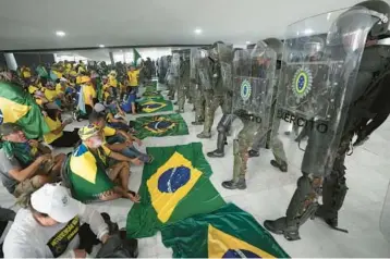  ?? ERALDO PERES/AP ?? Supporters of former President Jair Bolsonaro sit in front of police Jan. 8 inside the Planalto Palace in Brasilia, Brazil. While hundreds of civilians who took part in the riot have been jailed, service members have thus far been spared.