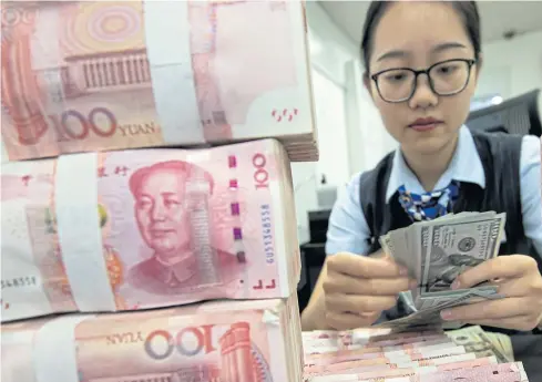  ?? CHINATOPIX VIA AP ?? A bank employee counts US banknotes next to stack of 100-yuan notes in Hai’an, Jiangsu province yesterday.