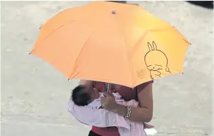  ?? PATIPAT JANTHONG ?? A woman holds baby and umbrella as she walks in Bangkok. The government is trying to encourage families to have more children as Thailand becomes an ageing society.