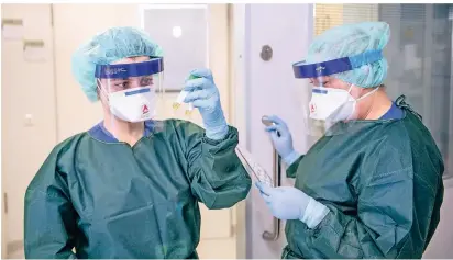  ?? FOTO: DPA ?? Zwei Bedienstet­e der Uniklinik Essen in Schutzklei­dung mit Abstrichrö­hrchen.