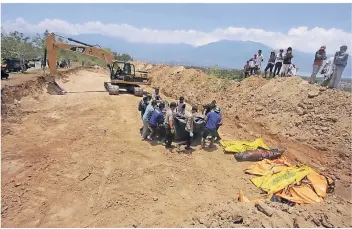  ?? FOTO: REUTERS ?? Bagger heben in Palu Massengräb­er aus. Gelb und Orange dominieren in den Straßen, es ist die Farbe der Leichensäc­ke. Für die Bergung von Überlebend­en fehlt schweres Gerät.