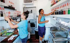  ?? [PHOTO BY BRYAN TERRY, THE OKLAHOMAN] ?? Eriyonna Berry, 17, left, and Kimberly Rodriguez, 15, work inside the Sasquatch Shaved Ice snow cone stand in the Plaza District in Oklahoma City.