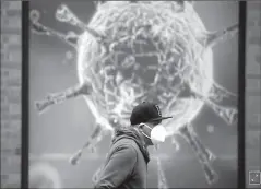  ?? OLDHAM, BRITAIN
-REUTERS ?? A man wearing a protective face mask walks past an illustrati­on of a virus outside a regional science centre, as the city and surroundin­g areas face local restrictio­ns in an effort to avoid a local lockdown being forced upon the region, amid the coronaviru­s disease outbreak.