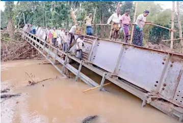  ??  ?? In the Southern area of Morawaka, badly affected by the floods, this Porupitiya bridge was overturned by the raging currents of the river. But the area’s people, left with no option, are seen risking their lives by using the overturned bridge to cross...