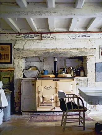  ??  ?? This farmhouse has natural, painted brickwork and exposed wooden beams. Antique wood furniture pieces are scattered throughout the kitchen, including built-in oak lintel cabinets that flank each side of the cream-colored Aga range cooker.