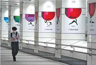  ??  ?? A man wearing a protective face mask walks next to wall decoration­s promoting the Olympics in Tokyo yesterday.