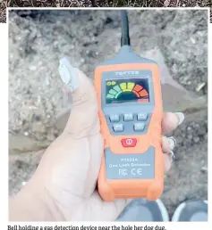  ?? ?? Bell holding a gas detection device near the hole her dog dug.