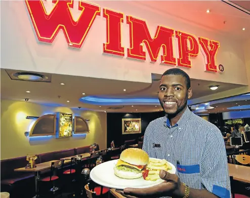  ?? Picture: Russell Roberts ?? A waiter serves up a hamburger at a Wimpy restaurant. After closures the group will still have 478 Wimpy outlets in SA.