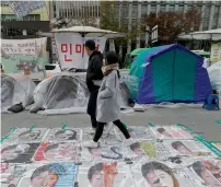  ?? AP ?? A couple walks on paintings criticisin­g President Park Geun-hye on a street in Seoul. —