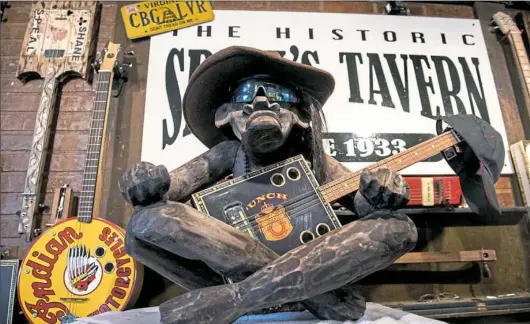  ?? Antonella Crescimben­i/Post-Gazette ?? Blu Magoo sits on top of an amp with a cigar box guitar in his lap in front of the 50 Cigar Box Guitars display at Speal’s Tavern in New Alexandria. The tavern has a display of three dozen handmade instrument­s.