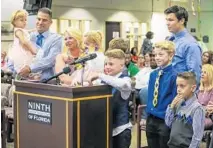  ??  ?? Adam Gruler holds 6-yearold Rachel and his wife, Jaimi, holds Rachel’s twin sister, Stephanie, as they stand before a judge Friday with their newly blended family that includes 8-year-old Jonathan, far right.