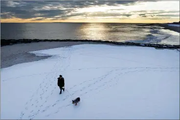  ?? PHOTO BY AL BELLO — GETTY IMAGES ?? A man walks his dog in Long Beach, N.Y., on Tuesday after a large winter storm passed through the area. Electricit­y demands are growing during winter months to power heaters as people move away from oil or gas furnaces.