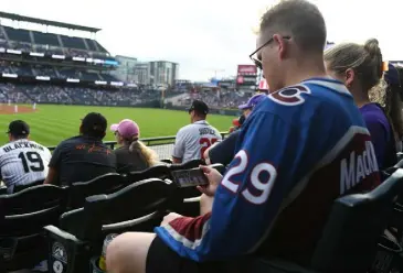  ?? RJ Sangosti, The Denver Post ?? Avalanche fan Garrett Harvey watches the hockey game on his phone while at Coors Field to see the Rockies on Thursday night.