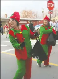  ?? Westside Eagle Observer/SUSAN HOLLAND ?? A pair of elves from Grand Savings Bank, dressed in holiday red and green, toss candy to youngsters in the crowd during the Gravette Christmas parade Saturday, Dec. 1. These two were among several entrants in the parade who distribute­d sweets to folks along the parade route and kept the youngsters scrambling to fill their pockets.