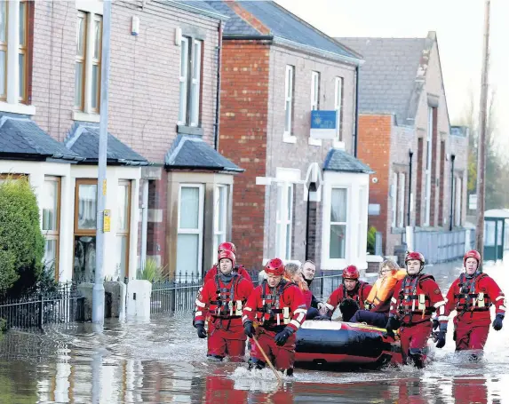  ?? Peter Byrne ?? > Rescue workers help residents to safety in Carlisle, after heavy rain from Storm Desmond tore through Britain, bringing strong winds and heavy rain