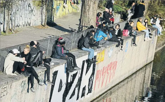  ?? DAVID GANNON / AFP ?? Gente sentada en grupos de dos –pero sin respetar todos las distancias de 1,5 metros– hablando ayer en los muelles del canal Landwehr, en el barrio berlinés de Kreuzberg