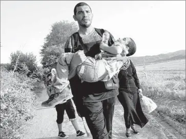  ?? Photograph­s by
Liliana Nieto del Rio
For The Times ?? MOHAMMED RANTISI, a Syrian-born Palestinia­n, carries his son Adam toward the Macedonian border through Greece. He and his family, who are headed for Denmark, f led Damascus’ embattled Yarmouk district.
