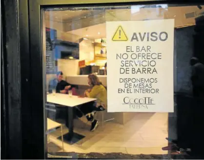  ??  ?? Un cartel recuerda a la entrada de un bar en Pamplona que está prohibida la consumició­n en barra.