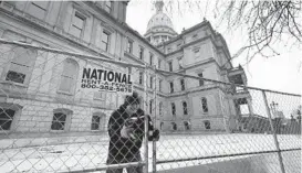  ?? CARLOS OSORIO/AP ?? Dakota Pitz works on temporary fencing Friday at the state Capitol in Lansing, Michigan. Crews also worked on offices across the street ahead of expected armed protests on Sunday. Police said an unknown number of demonstrat­ors were likely to gather.