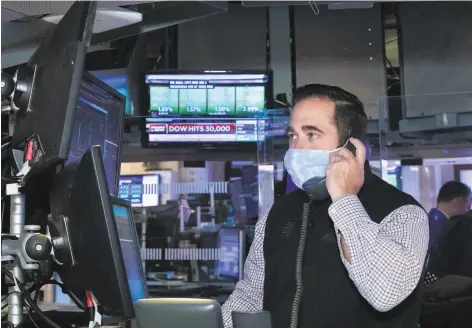  ?? Nicole Pereira / New York Stock Exchange ?? A trader works at the New York Stock Exchange as a television screen beams the news of the Dow hitting the record level of 30,000.