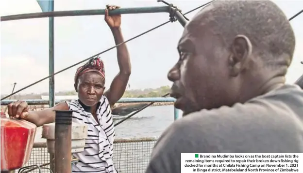  ?? ?? Brandina Mudimba looks on as the boat captain lists the remaining items required to repair their broken down fishing rig docked for months at Chilala Fishing Camp on November 1, 2021 in Binga district, Matabelela­nd North Province of Zimbabwe