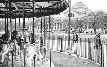  ?? BRENDAN SMIALOWSKI/GETTY-AFP ?? People pass an empty merry-go-round and the closed Smithsonia­n Natural History Museum on Saturday in Washington.