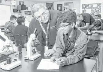  ?? Gary Fountain / For the Chronicle ?? Project Chrysalis Middle School principal Jose Covarrubia helps Kevin Fernando, a sixth-grade science student. The class is studying asexual reproducti­on through yeast samples.