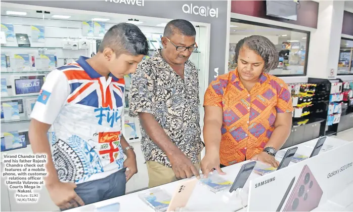  ?? Picture: ELIKI NUKUTABU ?? Virand Chandra (left) and his father Rajesh Chandra check out features of a mobile phone, with customer relations officer Ulamila Vulavou at Courts Mega in Nakasi.