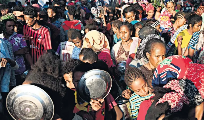  ??  ?? Ethiopian refugees, fleeing intense fighting in their homeland of Tigray, wait for food rations, below, at a border reception post in east Sudan