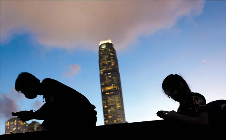  ?? (Reuters) ?? TWO PEOPLE look at their phones.