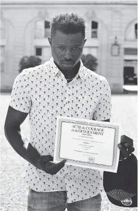  ?? THIBAULT CAMUS / AFP / GETTY IMAGES ?? Mamoudou Gassama displays a certificat­e of courage and dedication he received for scaling a Paris apartment building Saturday to save a boy dangling from a balcony.