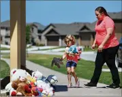  ?? ROSE BACA / DALLAS MORNING NEWS ?? Judith McDuffie, 4, places toys with her mother, Amanda McDuffie, Thursday at a memorial for a family that was slain Wednesday in Ponder.