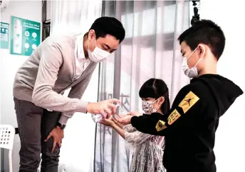  ??  ?? Kam (left) wears a face mask as he gives hand sanitiser to two of his students.