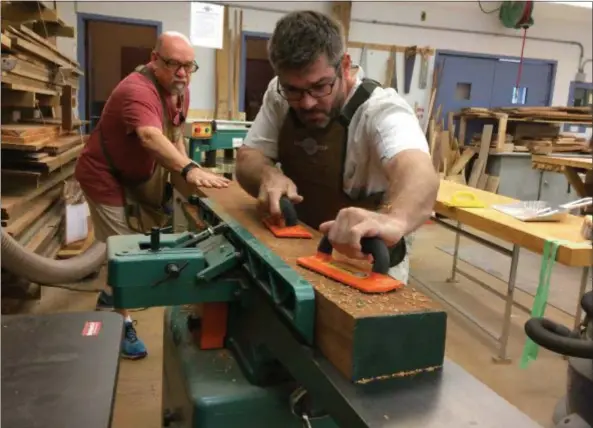  ?? CAROL HARPER — THE MORNING JOURNAL ?? Steve Waseleski, 68, of Lorain, left, and Shane Madey, 35, of Brook Park, establish an initial flat side on a board by running it through a jointer at North Coast Community Woodshop, a club for woodworker­s at 4214 Ivanhoe Ave. in Sheffield Lake.