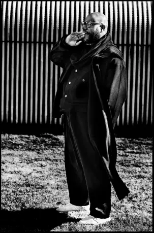  ??  ?? Steve McQueen wears black wool coat with attached scarf, £1,610; black gabardine jumpsuit, £2,870, both by Yohji Yamamoto. White leather trainers, McQueen’s own