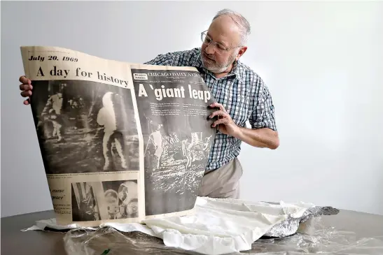  ?? Antonio Perez/ Chicago Tribune/TNS ?? Glen Williams, 65, opens up his preserved original July 21,1969, historic edition of the Chicago Daily News front page story on the moon landing on July 19 at the Chicago Tribune newspaper office. Williams was 15 years old when he and his mother, Edna Williams, followed the preservati­on instructio­ns on the newspaper's edition and stored it away for 50 years.