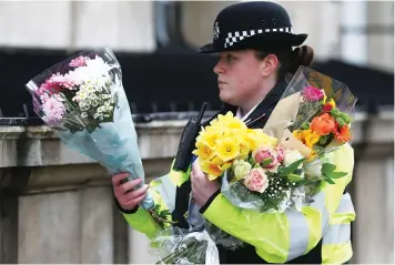  ?? (Reuters) ?? A POLICE OFFICER carries bouquets of flowers on Whitehall, the morning after the terrorist attack in London.