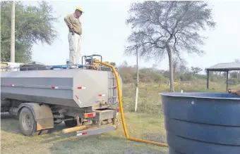  ??  ?? Personal de la empresa contratist­a encargada de reparar camino de tierra en la zona de Fuerte Olimpo provee de agua a la población. A los incendios se suma la escasez del vital líquido.