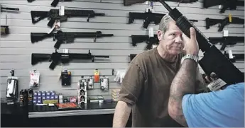  ?? Barbara Davidson Los Angeles Times ?? A GRAND TERRACE store owner, Frank Cobet, shows a customer a rifle days after the 2015 shootings in nearby San Bernardino. Many who buy in response to such attacks are new to gun ownership.