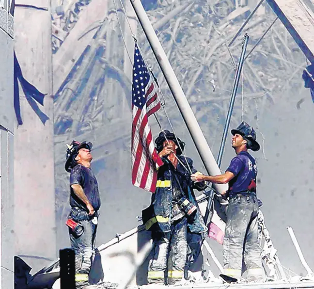  ??  ?? Firefighte­rs raise a flag late in the afternoon on Sept. 11, 2001, in the wreckage of the World Trade Center towers in New York. THOMAS E. FRANKLIN/THE RECORD