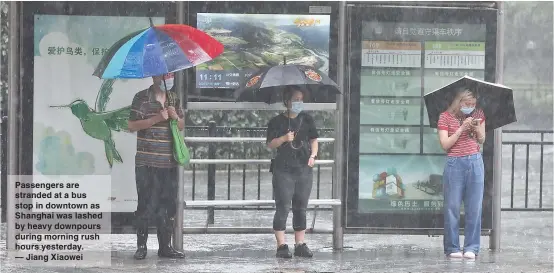  ??  ?? Passengers are stranded at a bus stop in downtown as Shanghai was lashed by heavy downpours during morning rush hours yesterday. — Jiang Xiaowei
