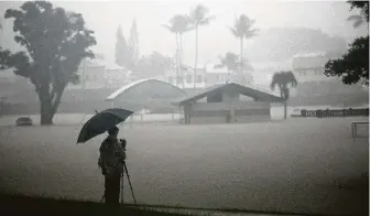  ?? Mario Tama / Getty Images ?? A man takes photos of floodwater­s from Hurricane Lane rainfall on Thursday in Hilo, Hawaii. Landslides on the easternmos­t major island have cut off the road that leads to Hilo.